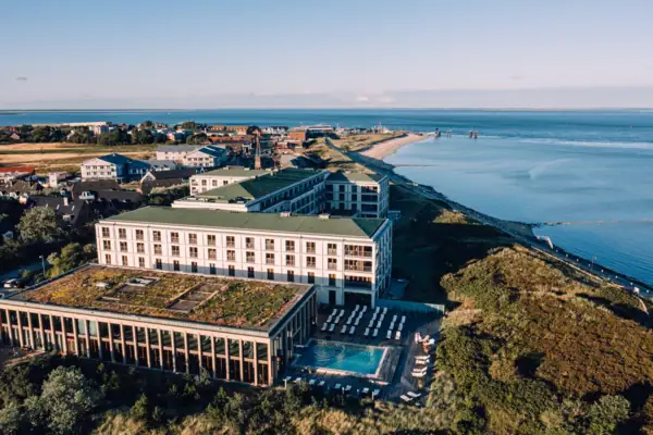 Das A-ROSA Hotel Sylt mit einem Pool und dem Strand mit der Nordsee im Hintergrund