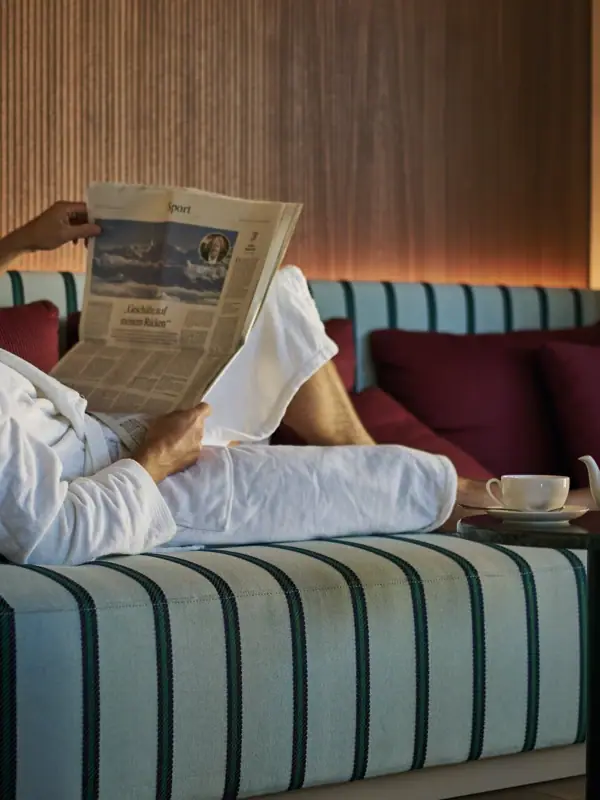 Ein Mann im Bademantel liest eine Zeitung auf einem Sofa.
