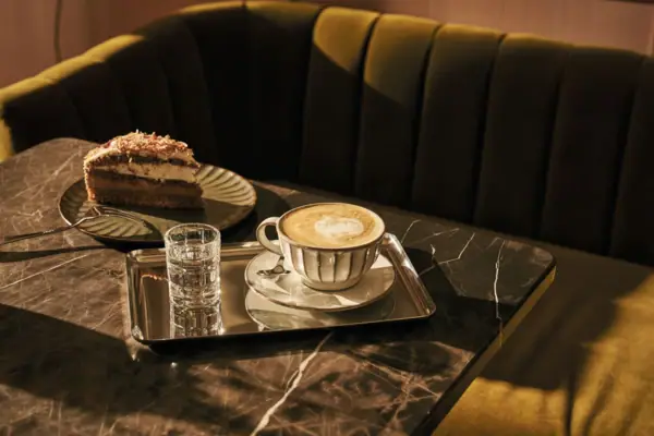 Ein Kaffeegedeck mit Kaffeetasse, Tortenstück und Gabel auf einem Tisch.