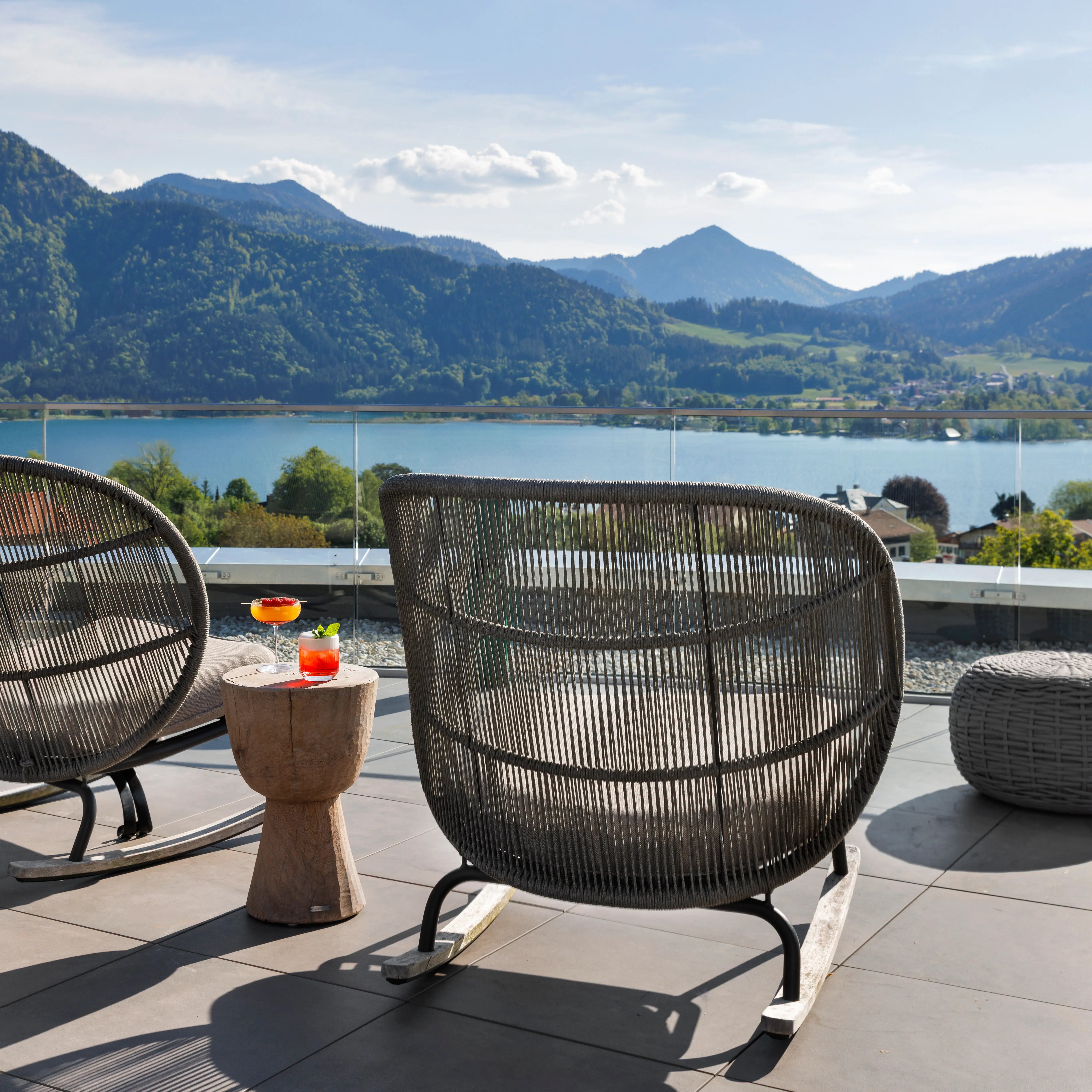 Die Terrasse vom A-ROSA Tegernsee it Sesseln und Drinks sowie dem spektakulärem Blick auf den Tegernsee und die Berge.