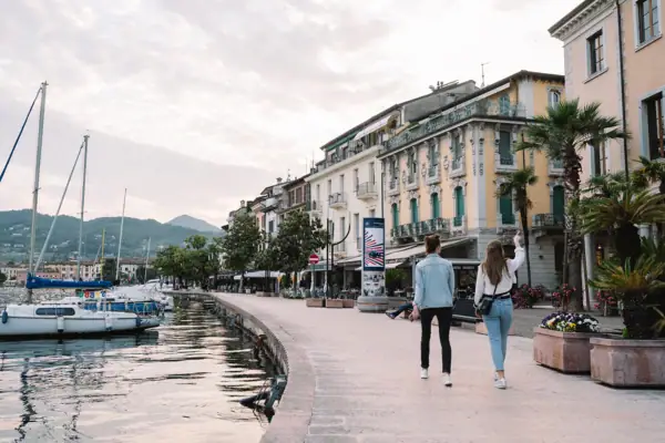 Zwei Frauen spazieren auf einem Gehweg neben dem Gardasee.