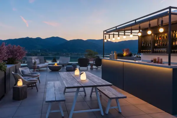 Terrasse mit Tisch und Stühlen vor einem See, im Hintergrund eine Bar.