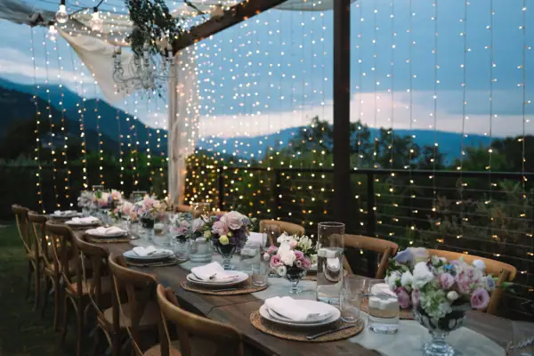 Festlich gedeckte Hochzeitstafel im Freien bei Nacht mit Lichterketten.