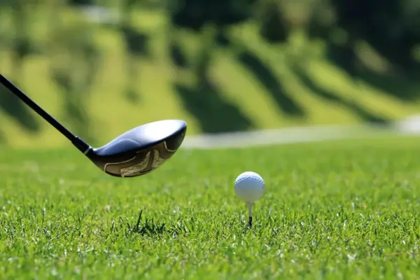 Golfschläger und Golfball auf einem Tee im Gras