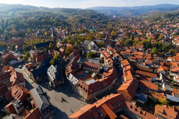 Luftaufnahme einer Stadt mit Häusern, Bäumen und Bergen im Hintergrund.
