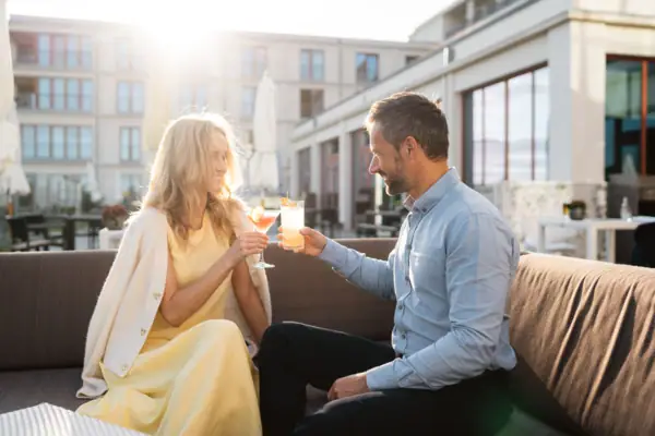 Ein Mann und eine Frau sitzen auf einem Sofa und halten Getränke in der Bar im A-ROSA Hotel Sylt.