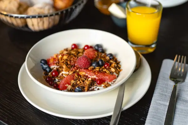 Eine Schale mit Obst und Müsli neben einem Glas Saft.