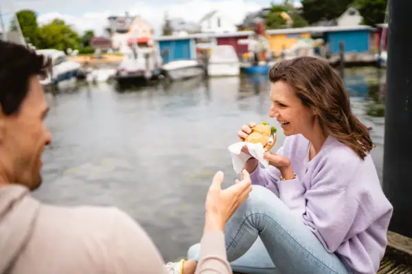 Eine Frau sitzt auf einem Steg und isst einen Burger.