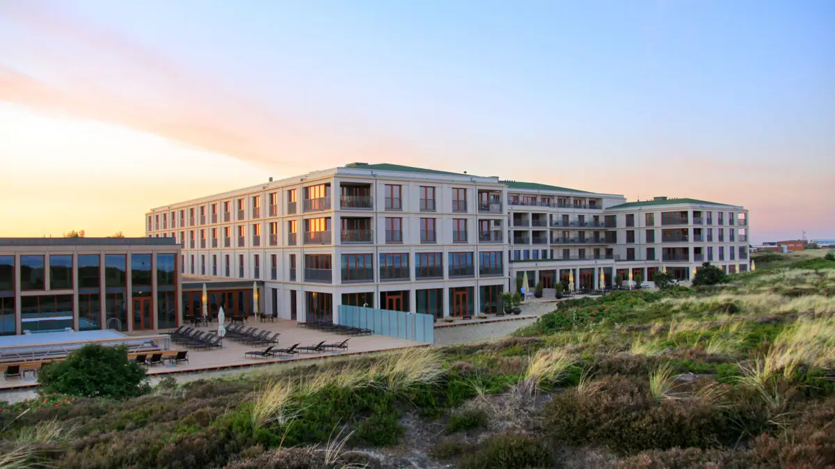 Das A-ROSA Hotel Sylt mit Rasen und Stühlen im Freien bei Sonnenaufgang.