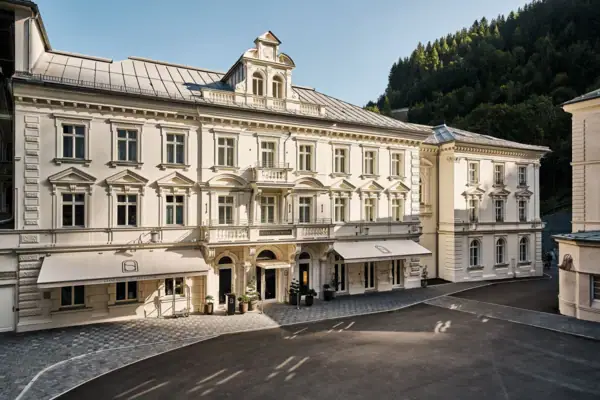 Großes weißes Gebäude mit Fenstern und gepflastertem Bereich im Vordergrund.