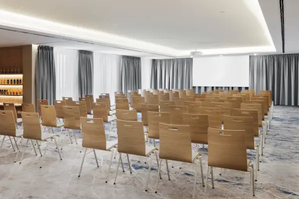 Der Konferenzraum 1 im A-ROSA Tegernsee mit Stuhlreihen und einem Beamer und einer Leinwand.
