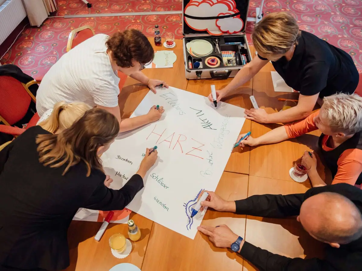 Eine Gruppe von Menschen sitzt um einen Tisch und schreibt auf ein großes Papier.