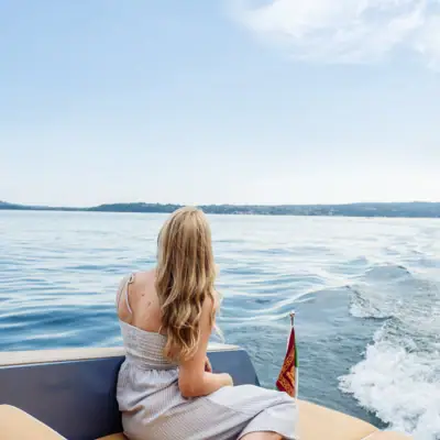 Eine Frau sitzt auf einem Boot. Das Boot fährt auf dem Gardasee. Die Frau schaut in die Ferne.
