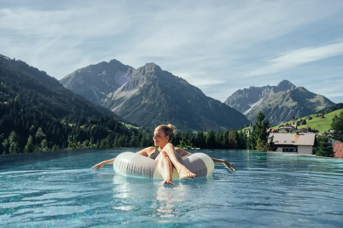 Eine Frau treibt auf einem Schwimmreifen in einem Pool mit Bergen im Hintergrund.