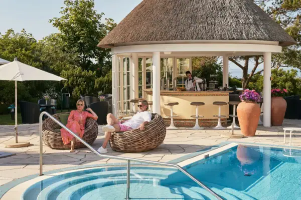 Ein Mann und eine Frau sitzen in Korbstühlen neben einem Pool.