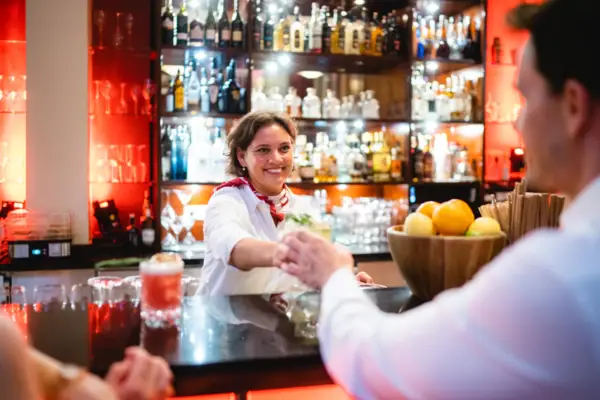 Eine Frau reicht einem Mann hinter einer Bar ein Getränk über die Theke.