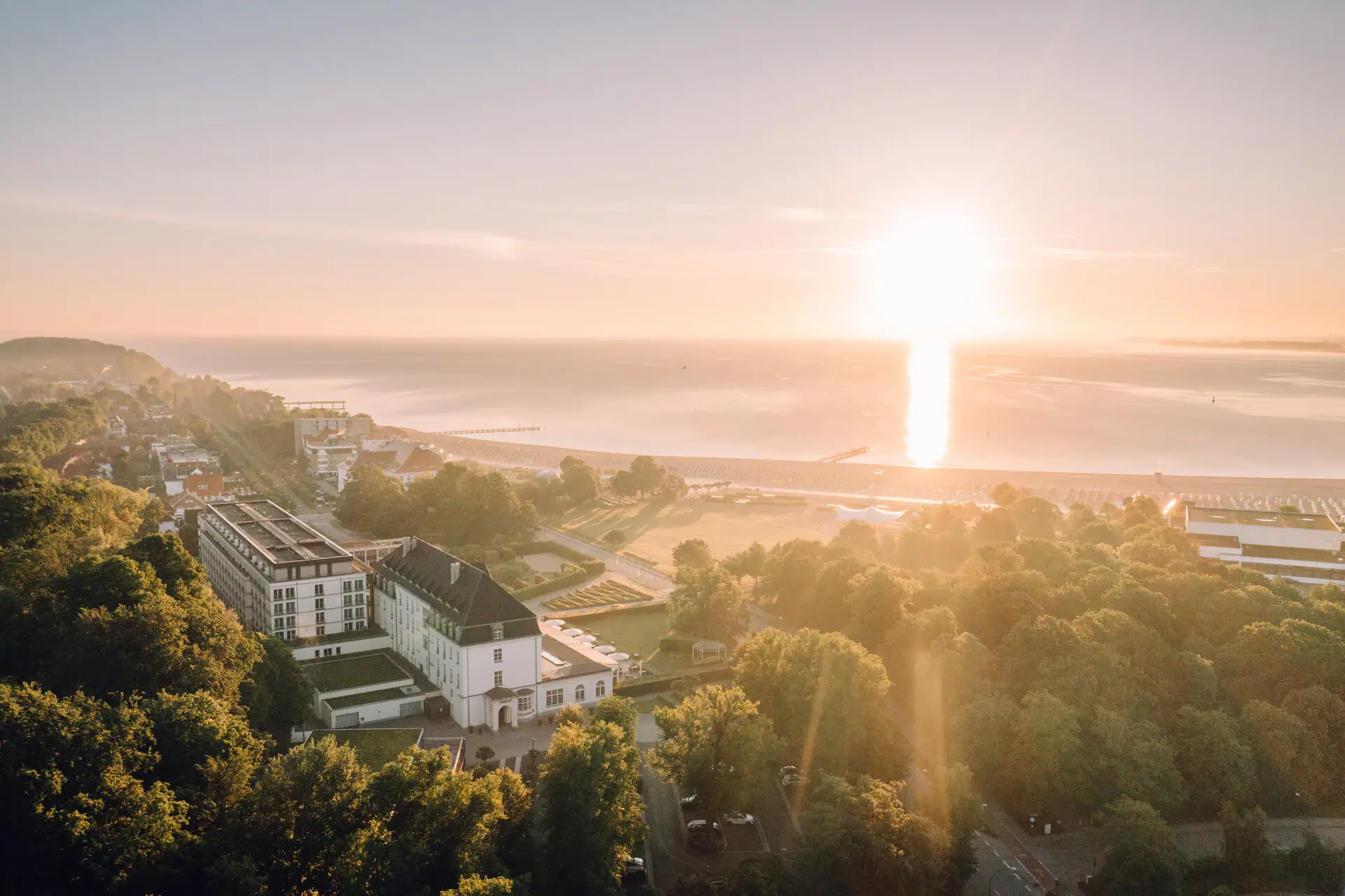 Stadt mit Bäumen und einem Gewässer bei Sonnenaufgang.