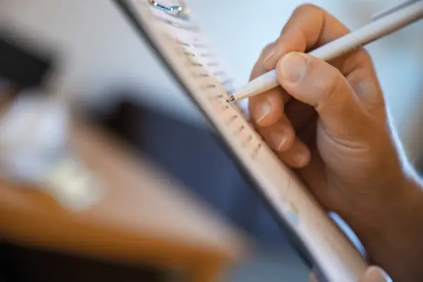 Eine Person schreibt mit einem Stift auf einem Klemmbrett.
