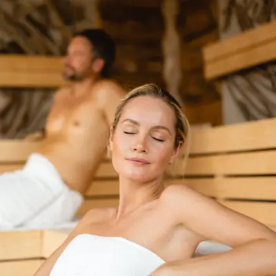 sauna und entspannung Eine Frau sitzt in einer Sauna, ein Mann im Hintergrund.