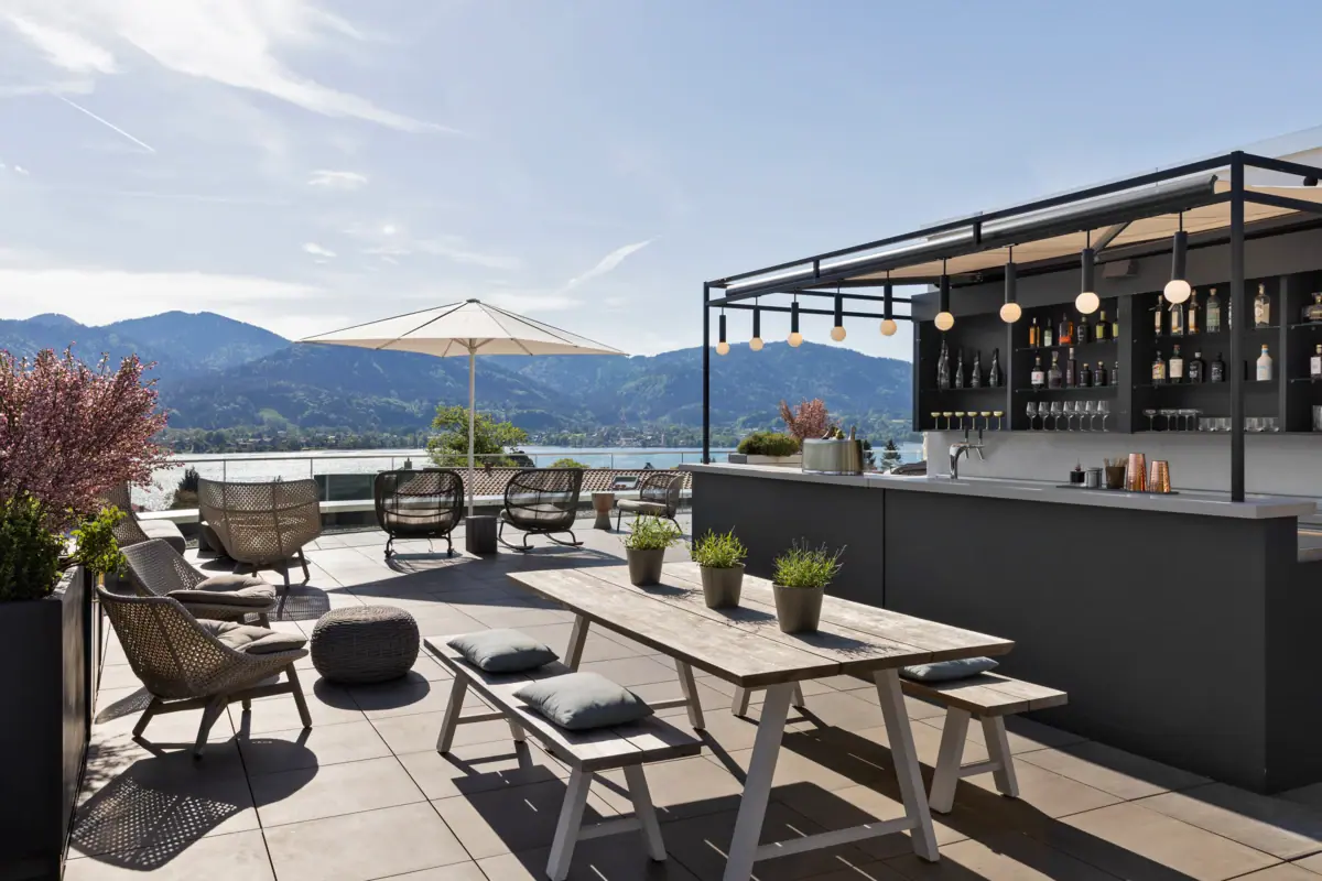 Rooftop-Terrasse mit Bar, Stühlen, Tisch und Sonnenschirm.