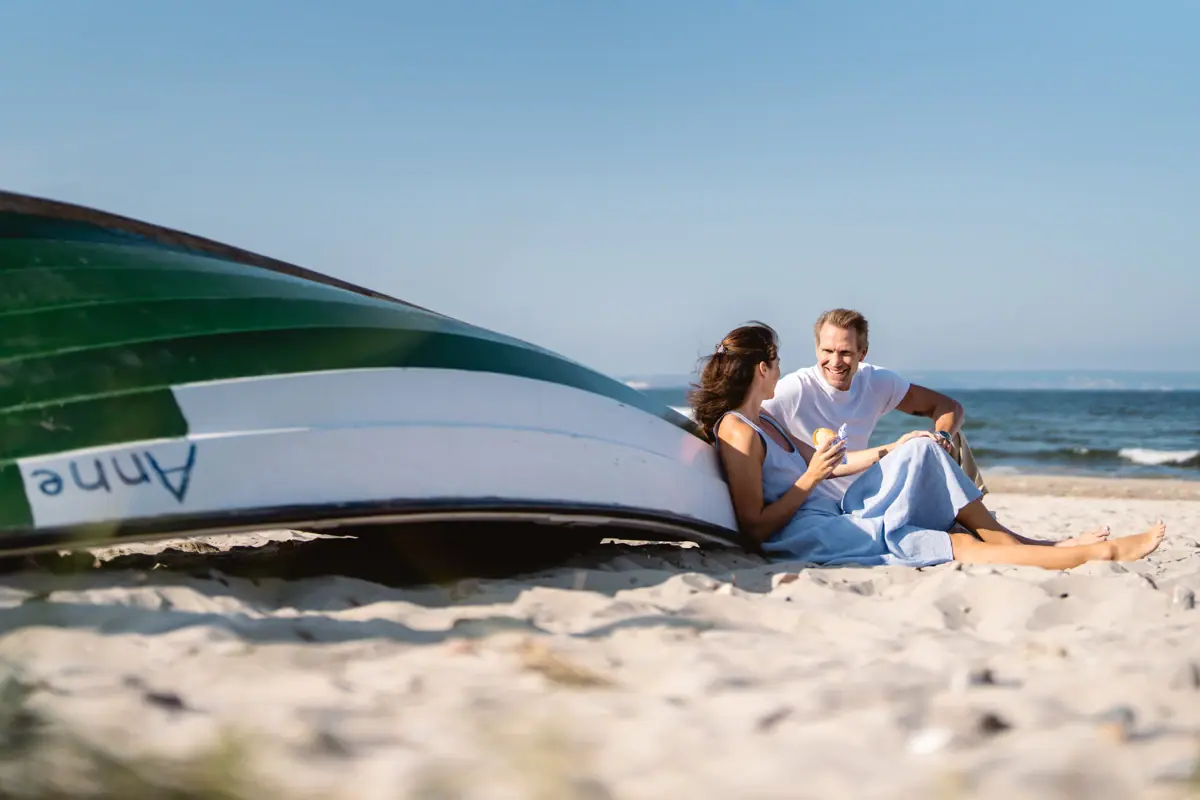 Ein Mann und eine Frau sitzen am Strand neben einem Boot.