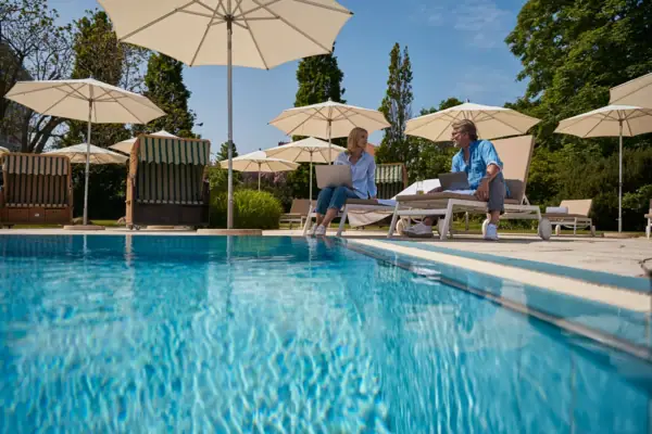 Ein Mann und eine Frau sitzen auf Liegestühlen am Pool.