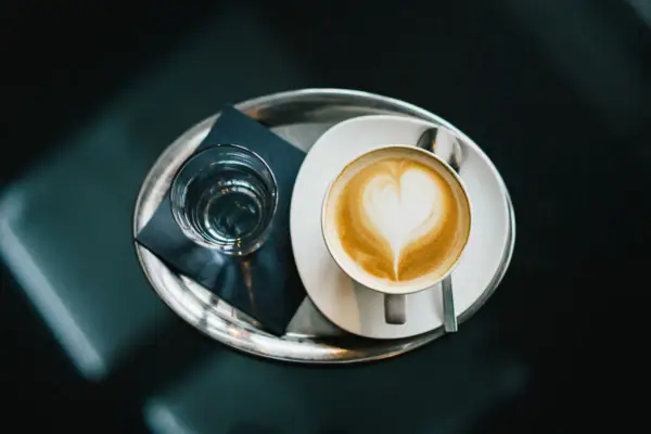 Eine Tasse Kaffee mit herzförmigem Milchschaum auf einem weißen Teller.