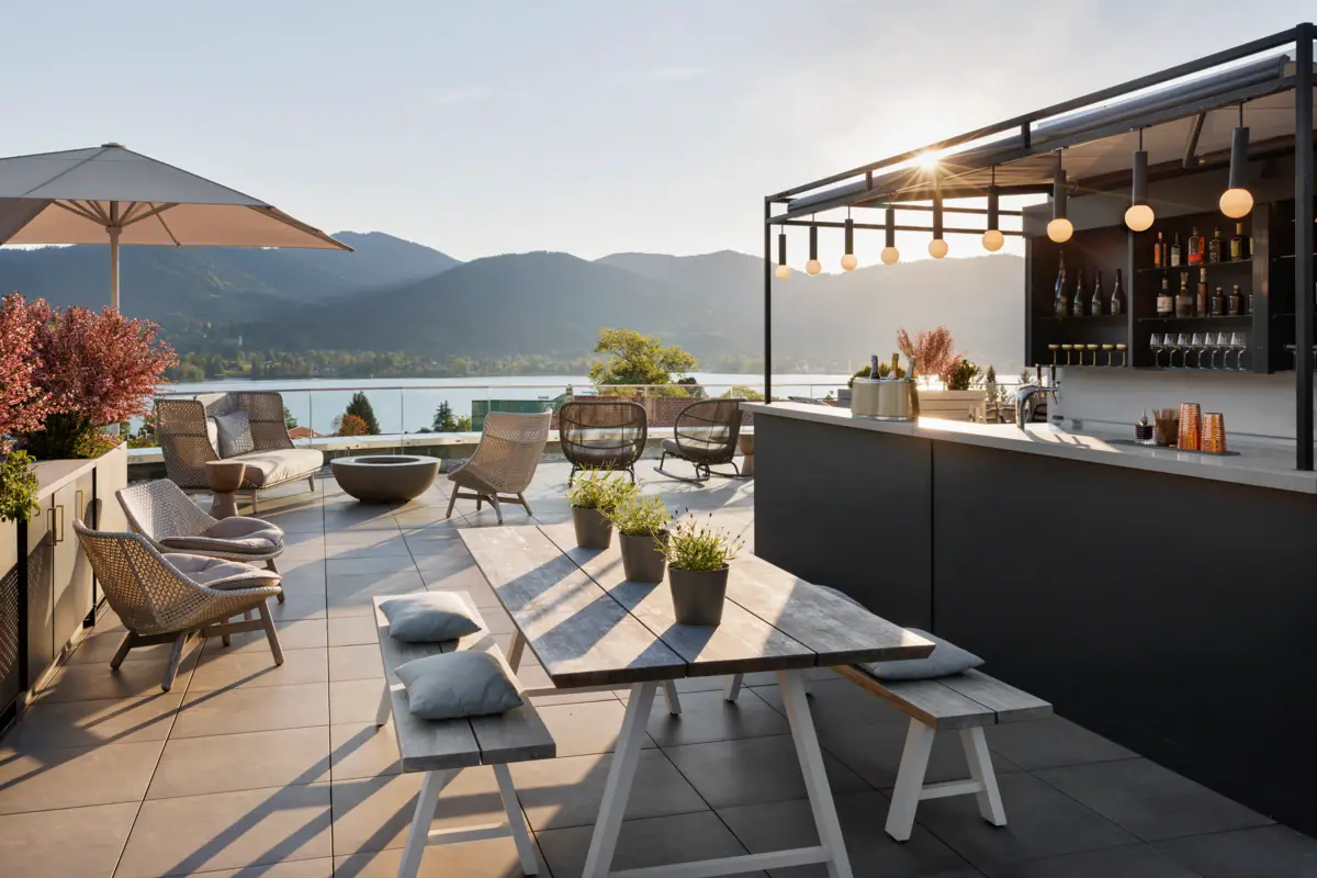 Terrasse mit Tisch und Stühlen, Bar und Blick auf einen See.
