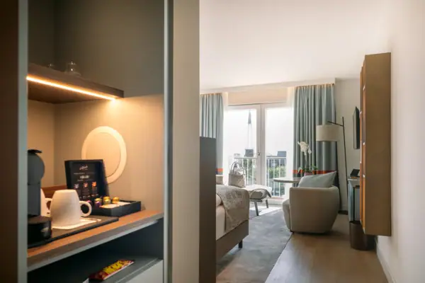 Ein Hotelzimmer mit einer Kaffeemaschine, einem Sessel, großen Fenstern, einem Fernseher und einem Bett.