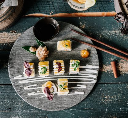 Auf einem dunklen Teller sind einzelne Sushi Häppchen hübsch angerichtete und mit Soße verziert.